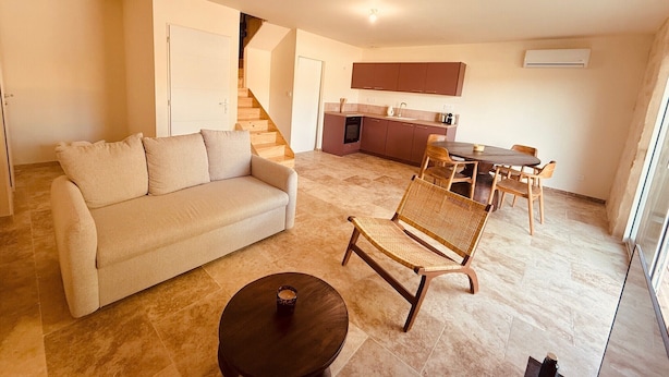 Een woonkamer met een bank, een eettafel met stoelen, een keuken en een trap.