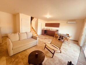 Un soggiorno con divano, un tavolo da pranzo con sedie, una zona cucina e una scala.