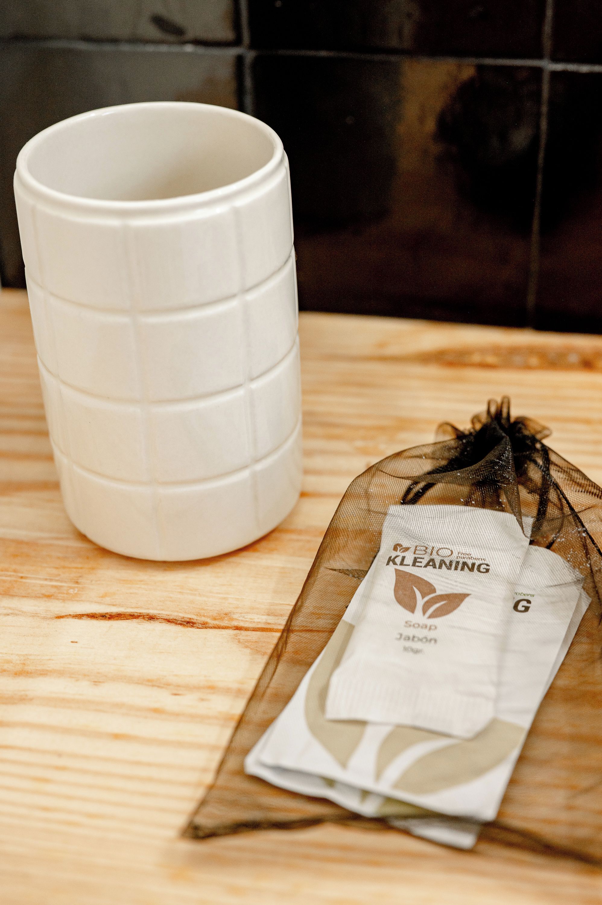 Uma caneca de cerâmica branca e um saquinho de sabonete sobre uma superfície de madeira.