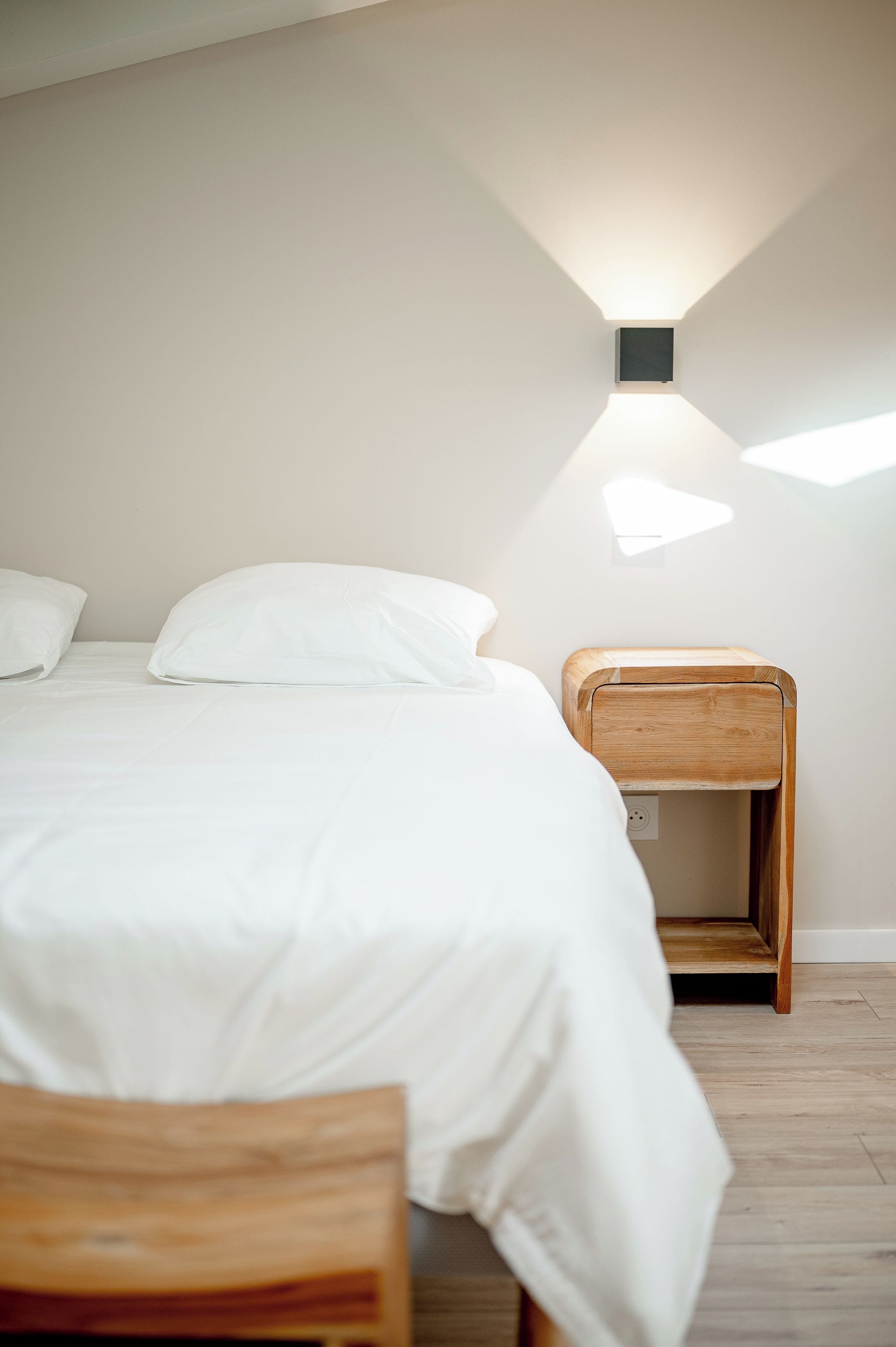 A bedroom with a bed, a nightstand, and a wall-mounted light fixture.