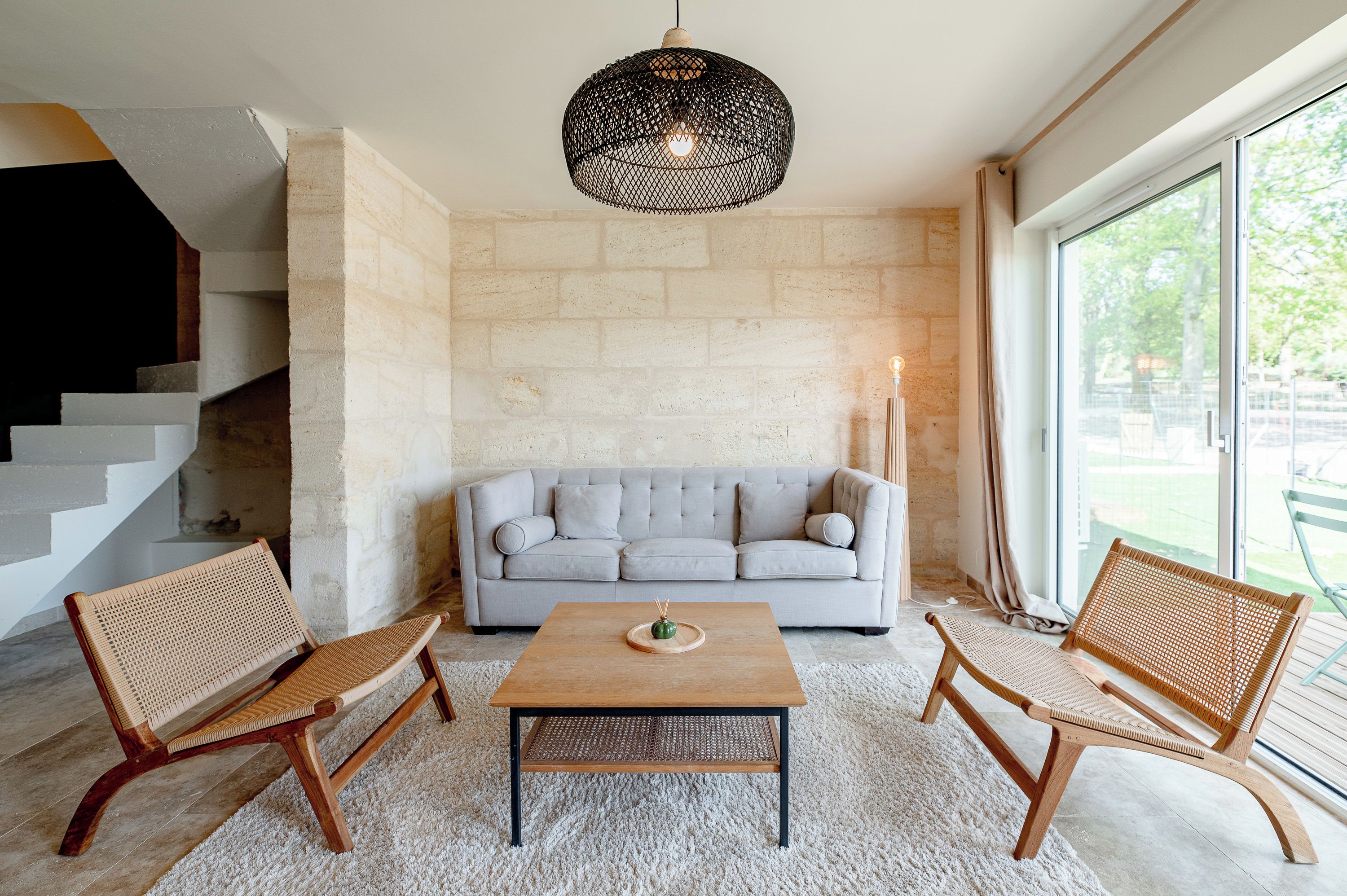 Uma sala de estar moderna com um sofá, duas cadeiras de vime, uma mesa de centro e um lustre.