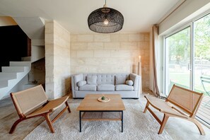 Una sala de estar moderna con un sofá, dos sillones de mimbre, una mesa de centro y una lámpara colgante.