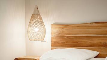 A neatly made bed with white linens, a wooden headboard, and a woven light fixture above it.