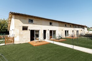A two-story building with a flat roof and a paved patio area with outdoor furniture. - Le Chai de Canteloup (Yvrac)