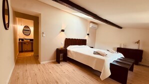 Een slaapkamer met een bed, nachtkastjes, een bankje, een spiegel en een airconditioning.