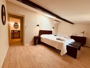 A bedroom with a bed, bedside tables, a bench, a mirror, and an air conditioning unit.