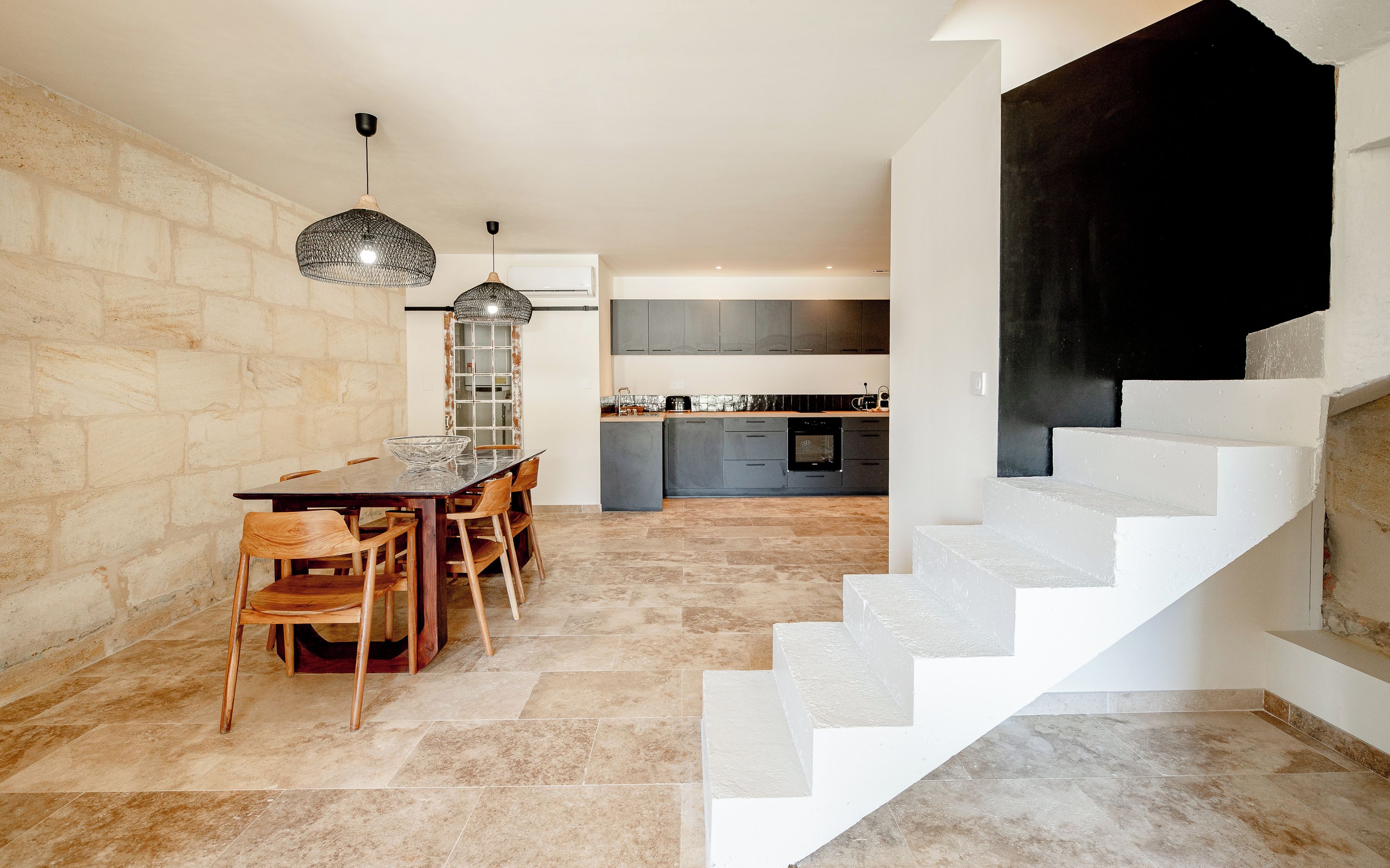 A modern kitchen with grey cabinets, a dining table with chairs, and a staircase with white steps.