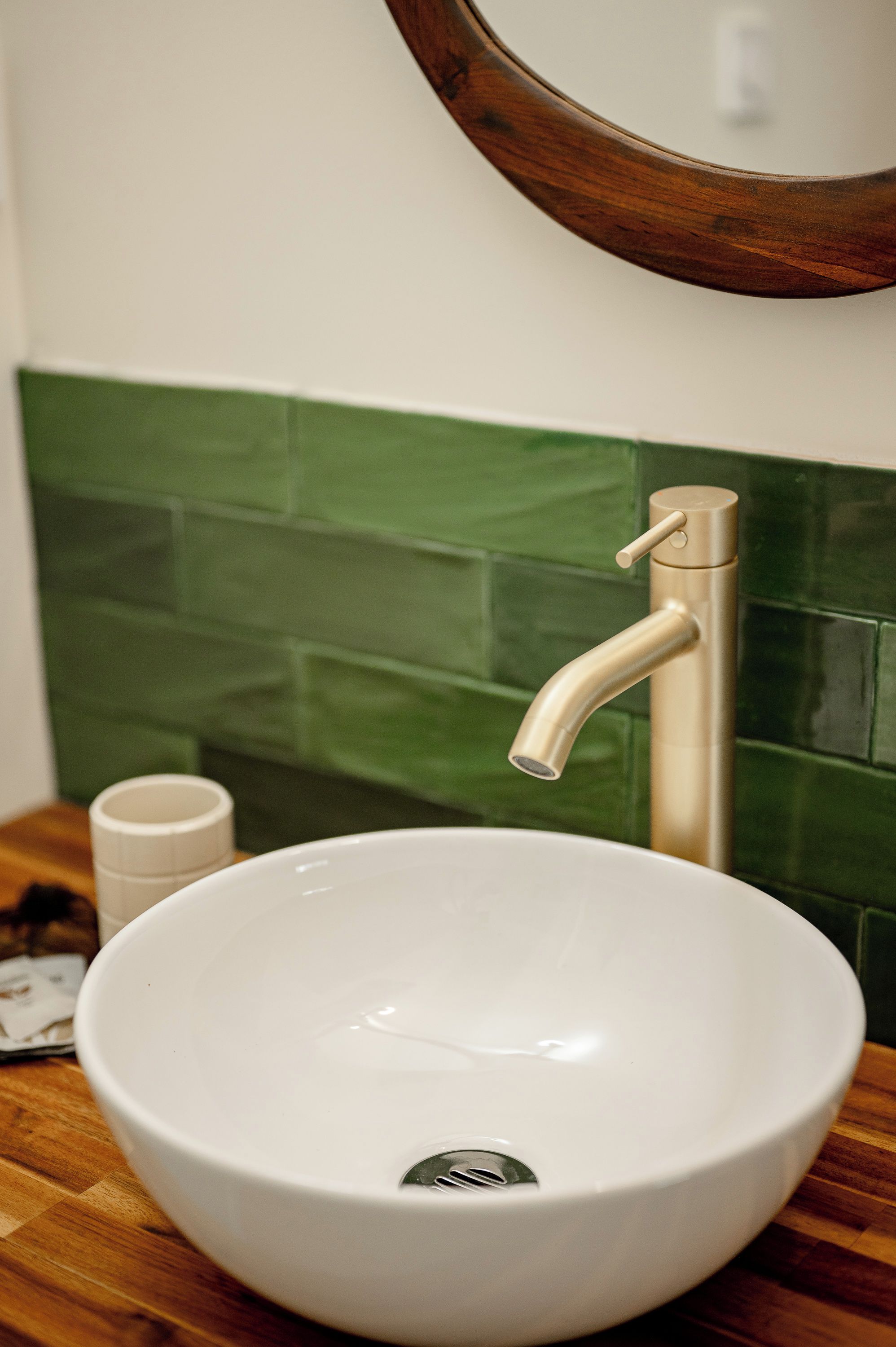 A white ceramic sink with a single faucet, set against a green tiled wall.