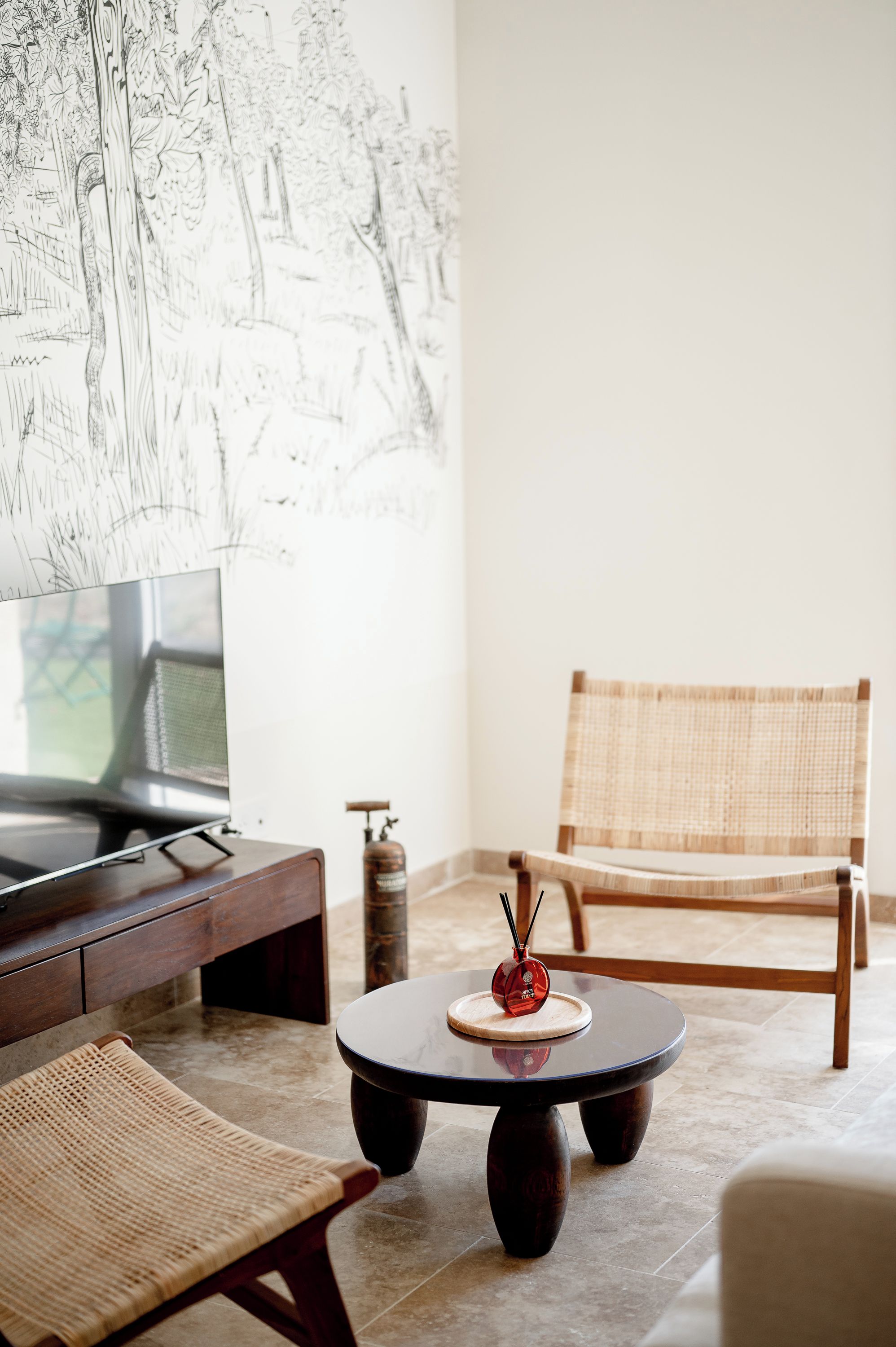 A modern living room with a television, a round coffee table with a red decorative item, a wicker chair, and a wall-mounted artwork.