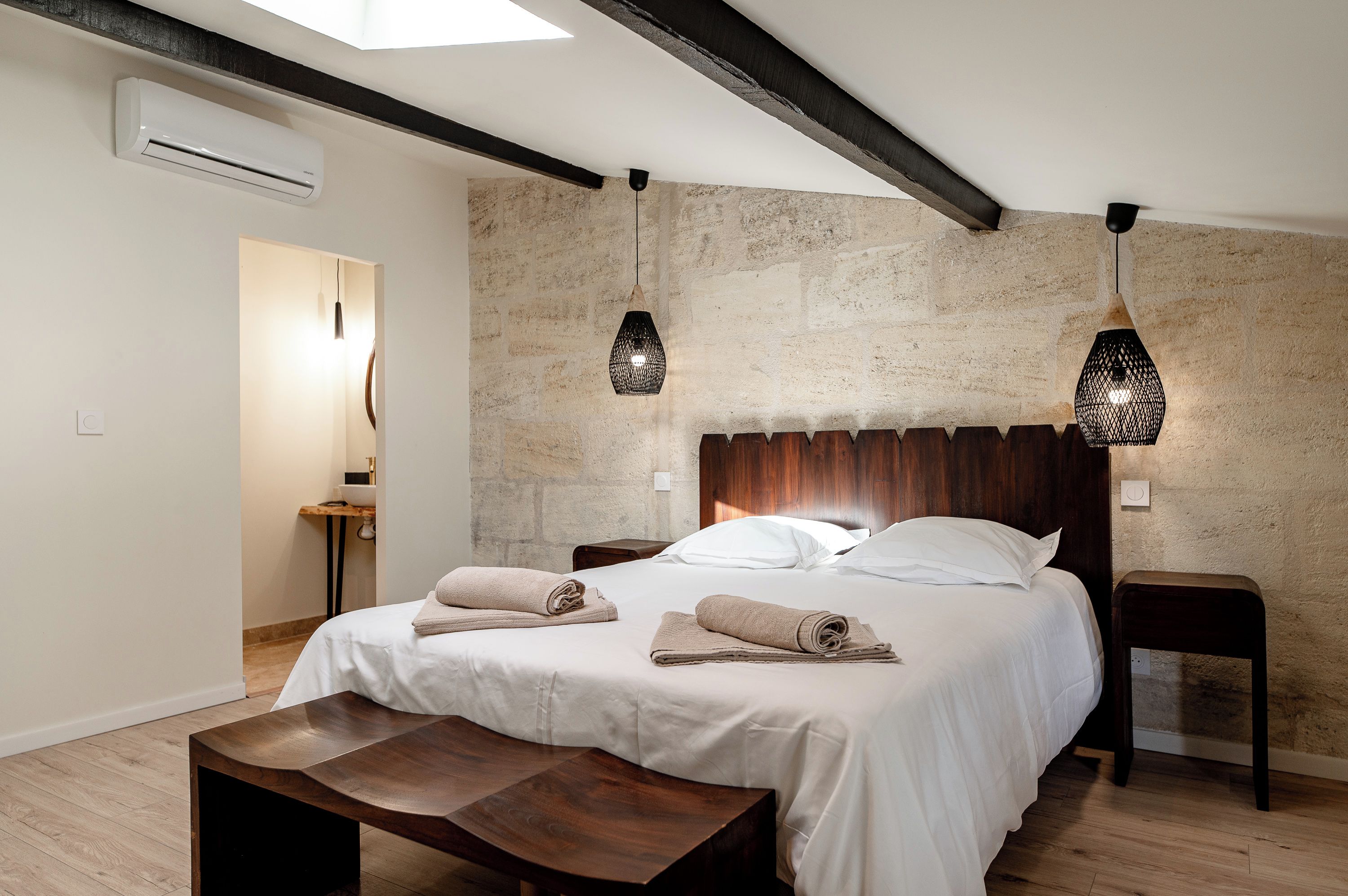A bedroom with a bed, bedside tables, a bench, and hanging lamps.