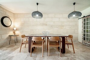 A dining area with a rectangular table, six wooden chairs, two hanging pendant lights, a round mirror, and a small side table with a lamp. - Le Chai de Canteloup (Yvrac)