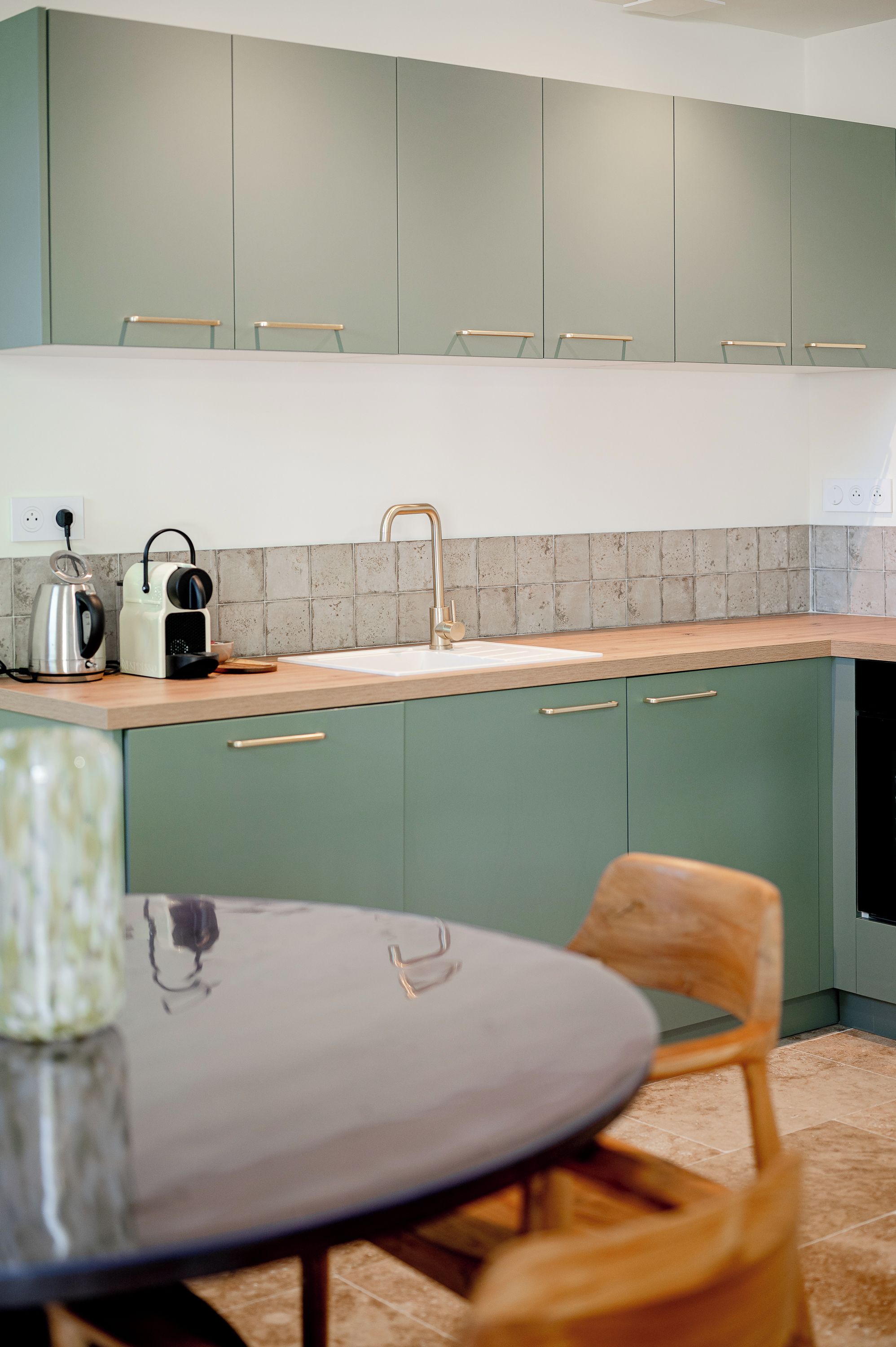 Een moderne keuken met groene kastjes, een wit aanrecht en een houten eettafel.