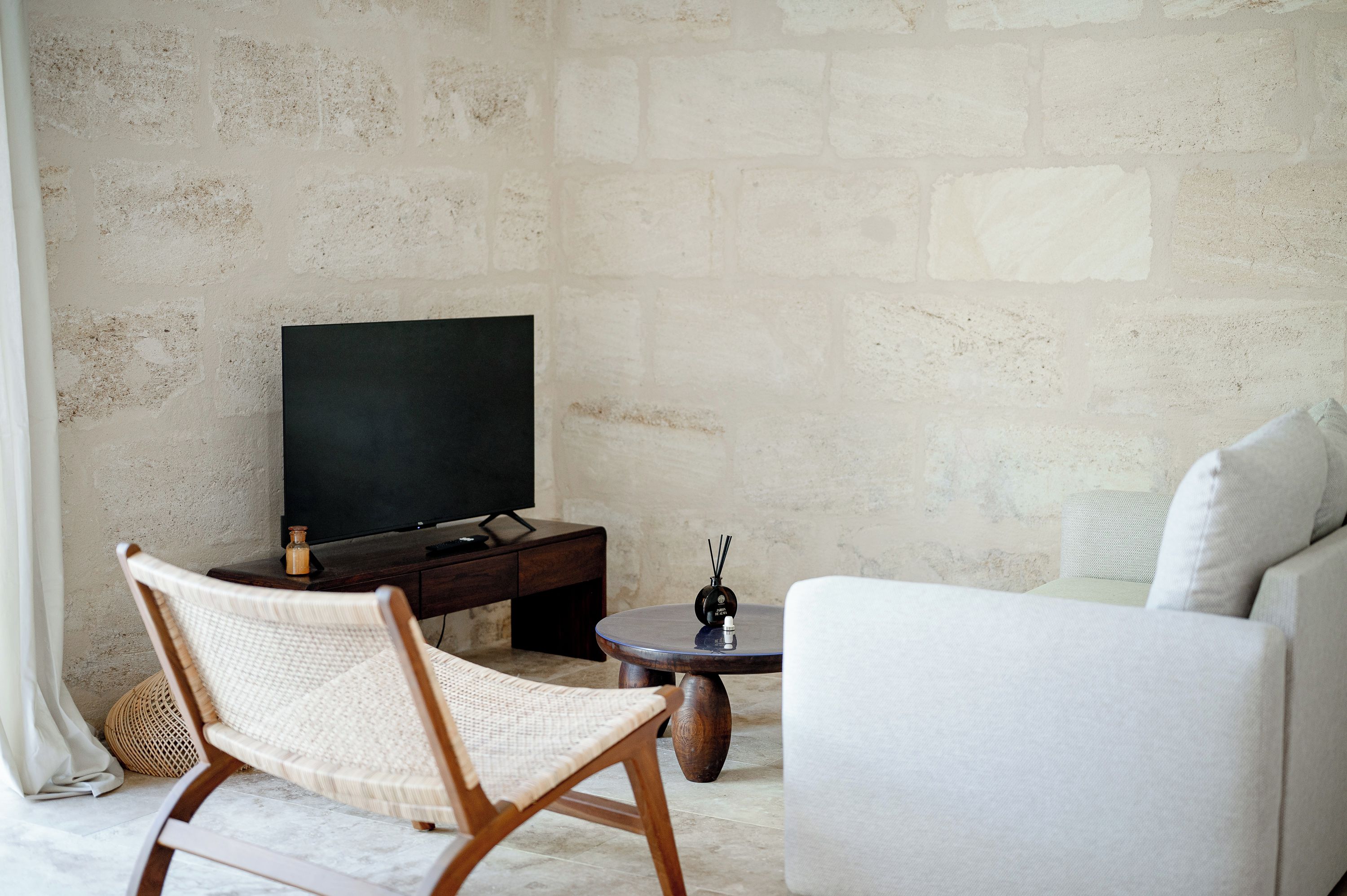 A living room with a television, a wicker chair, a white sofa, and a small table with a decorative item.