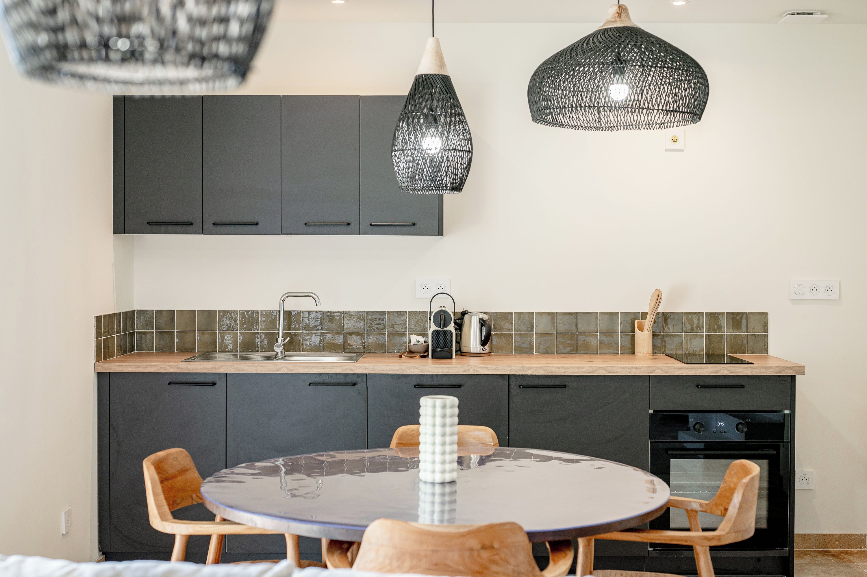 A modern kitchen with dark cabinets, a round table, and two pendant lights.