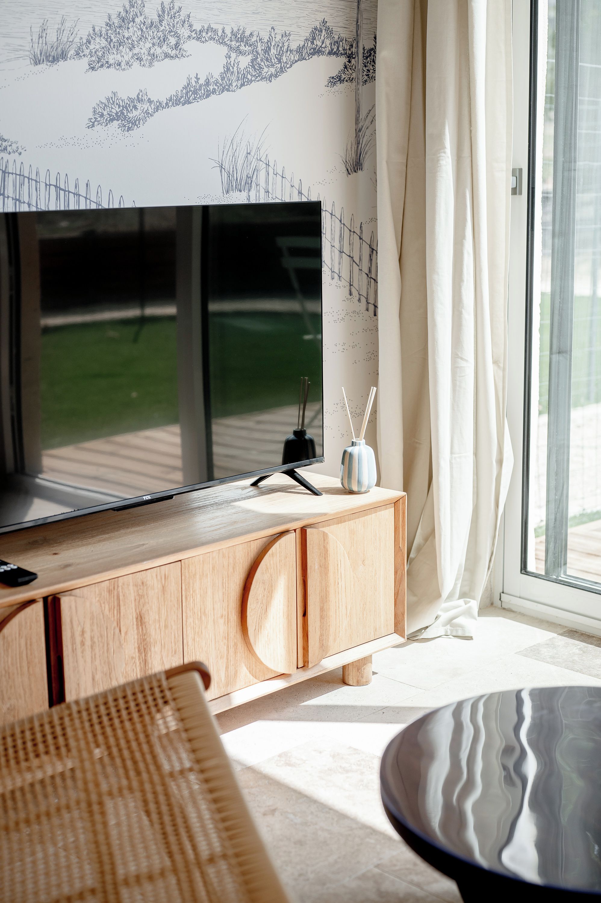 Un salon moderne doté d’un téléviseur à écran plat, d’un meuble en bois et d’une porte en verre donnant sur un espace extérieur.