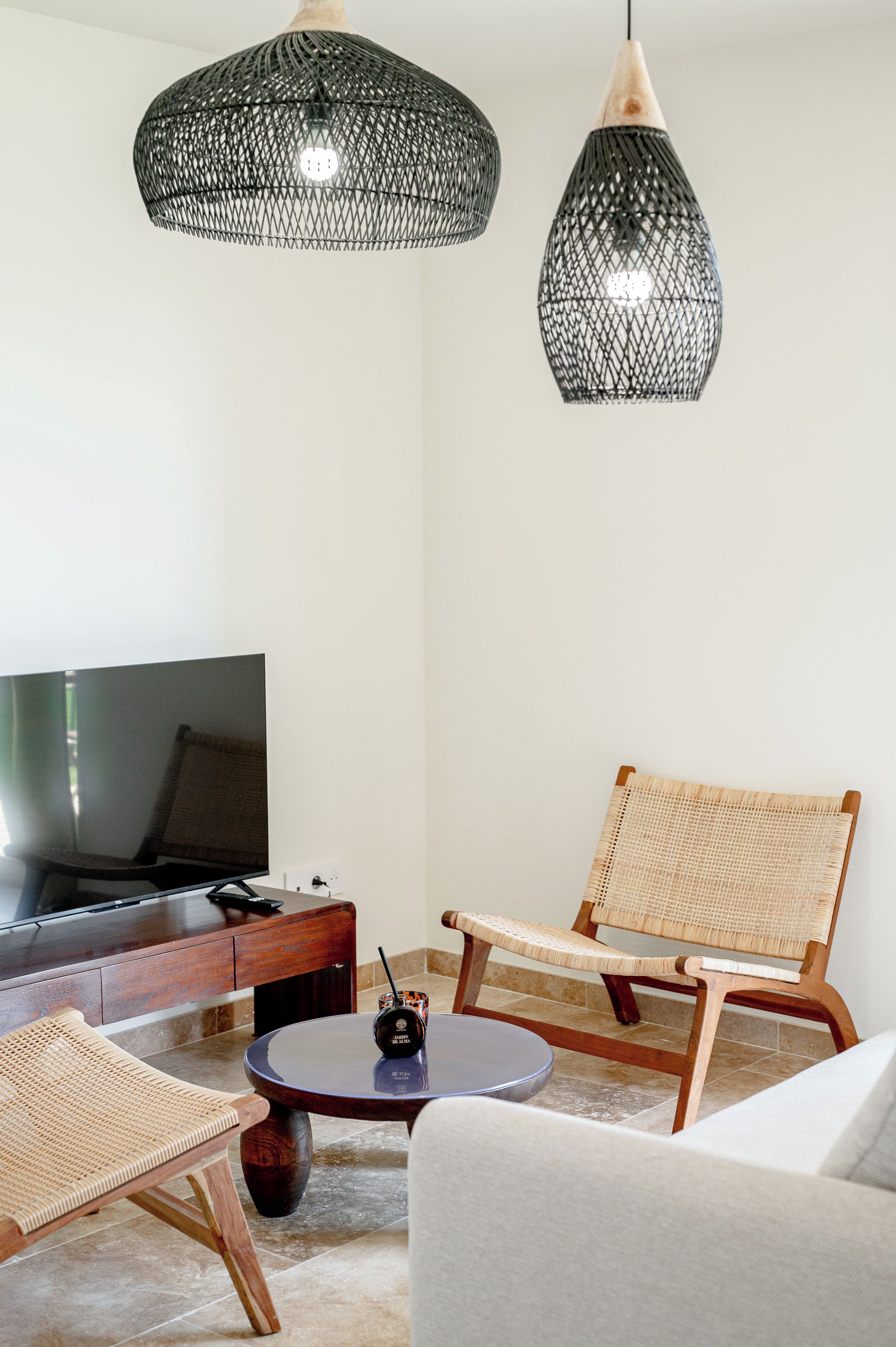 Una sala de estar moderna con televisor, muebles de mimbre y dos lámparas colgantes.