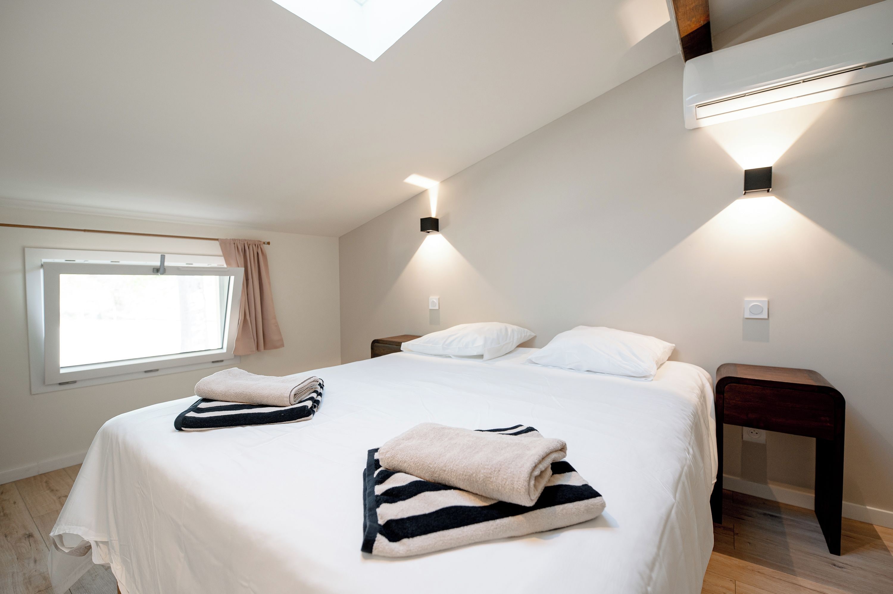 A bedroom with a bed, two bedside tables, a window with curtains, and a ceiling light fixture.