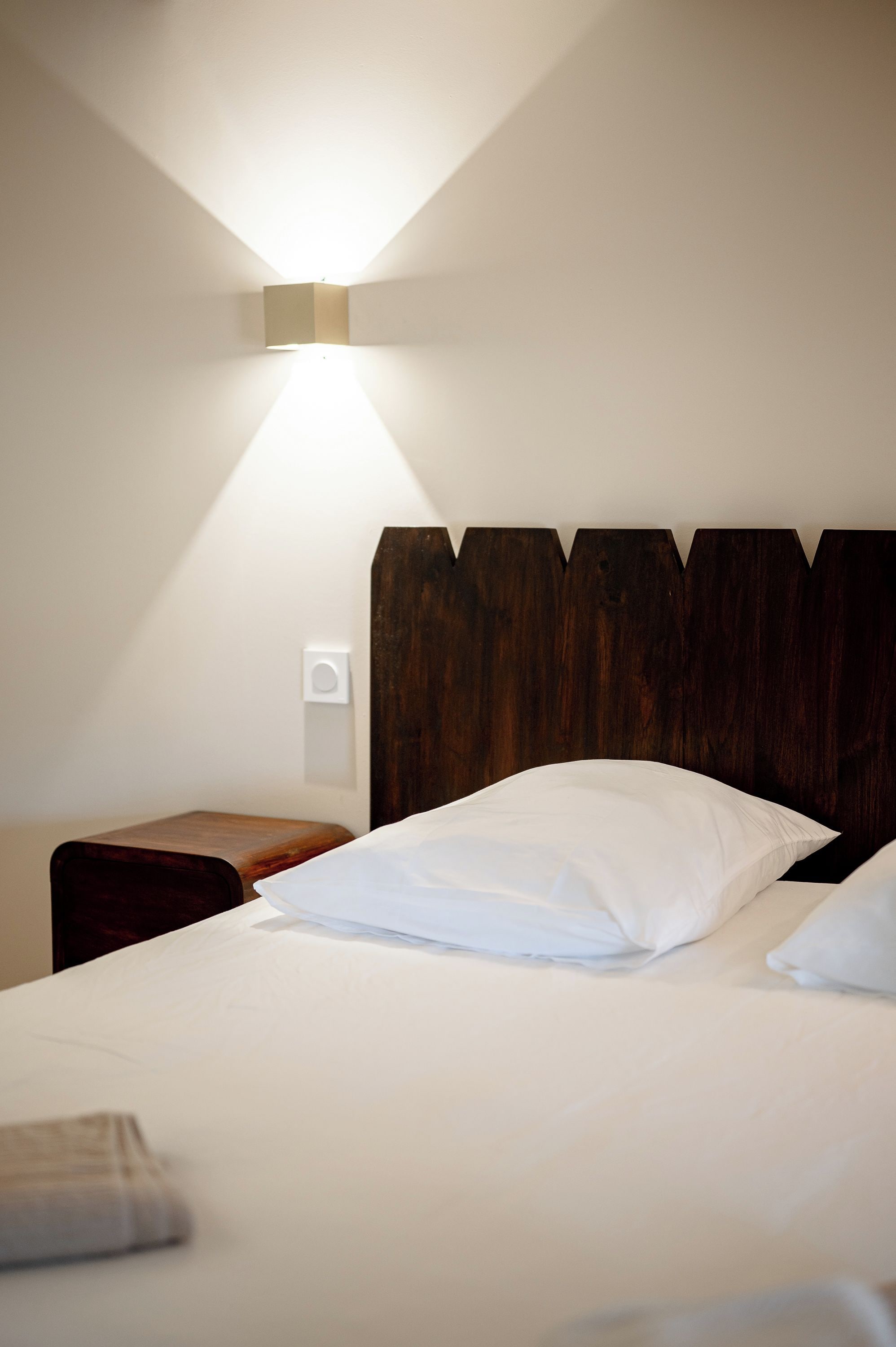 A hotel room with a bed, a bedside table, and a wall-mounted light fixture.