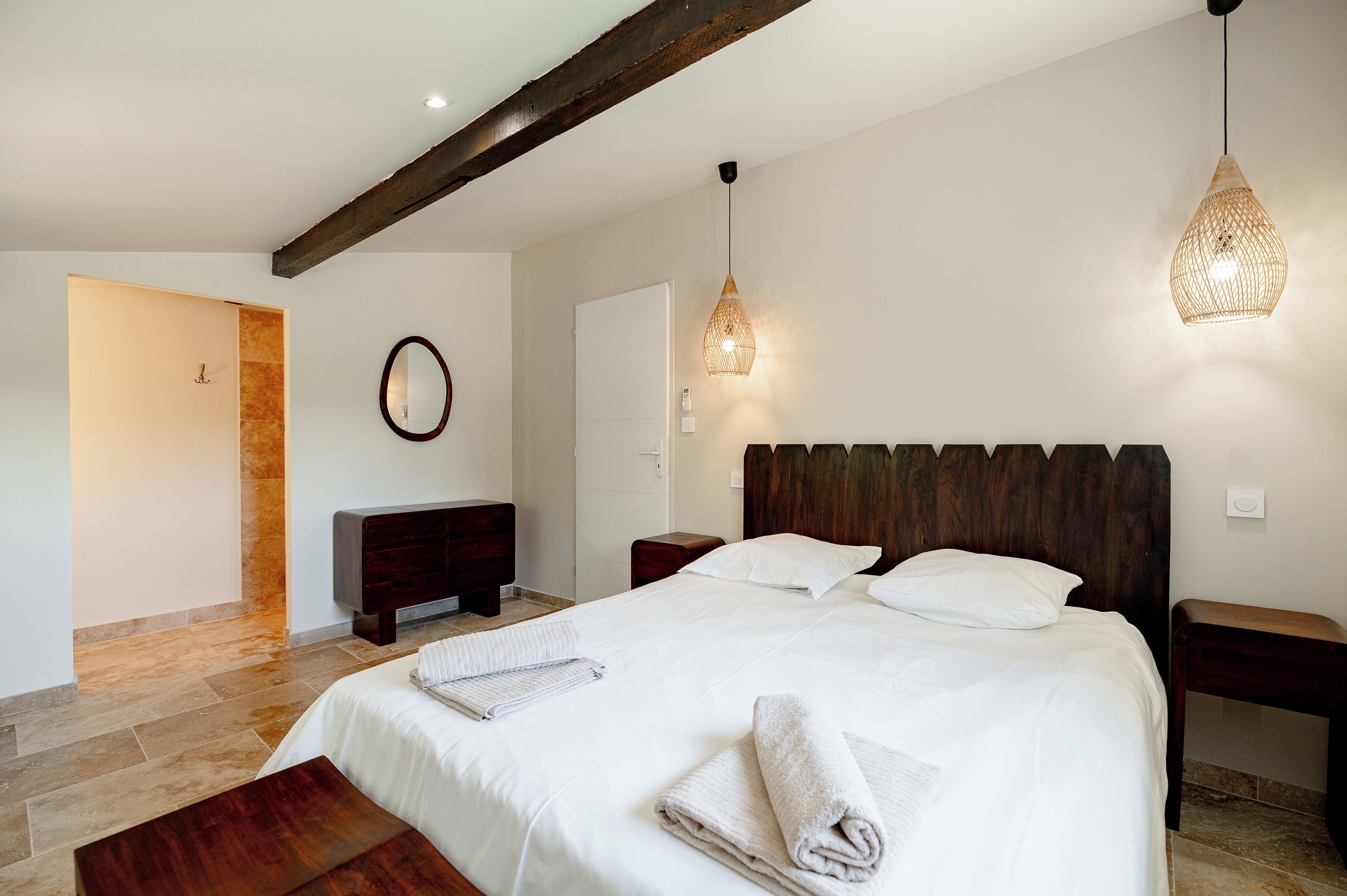 Un dormitorio con una cama grande, cabecera de madera, mesitas de noche, un espejo y dos lámparas colgantes.