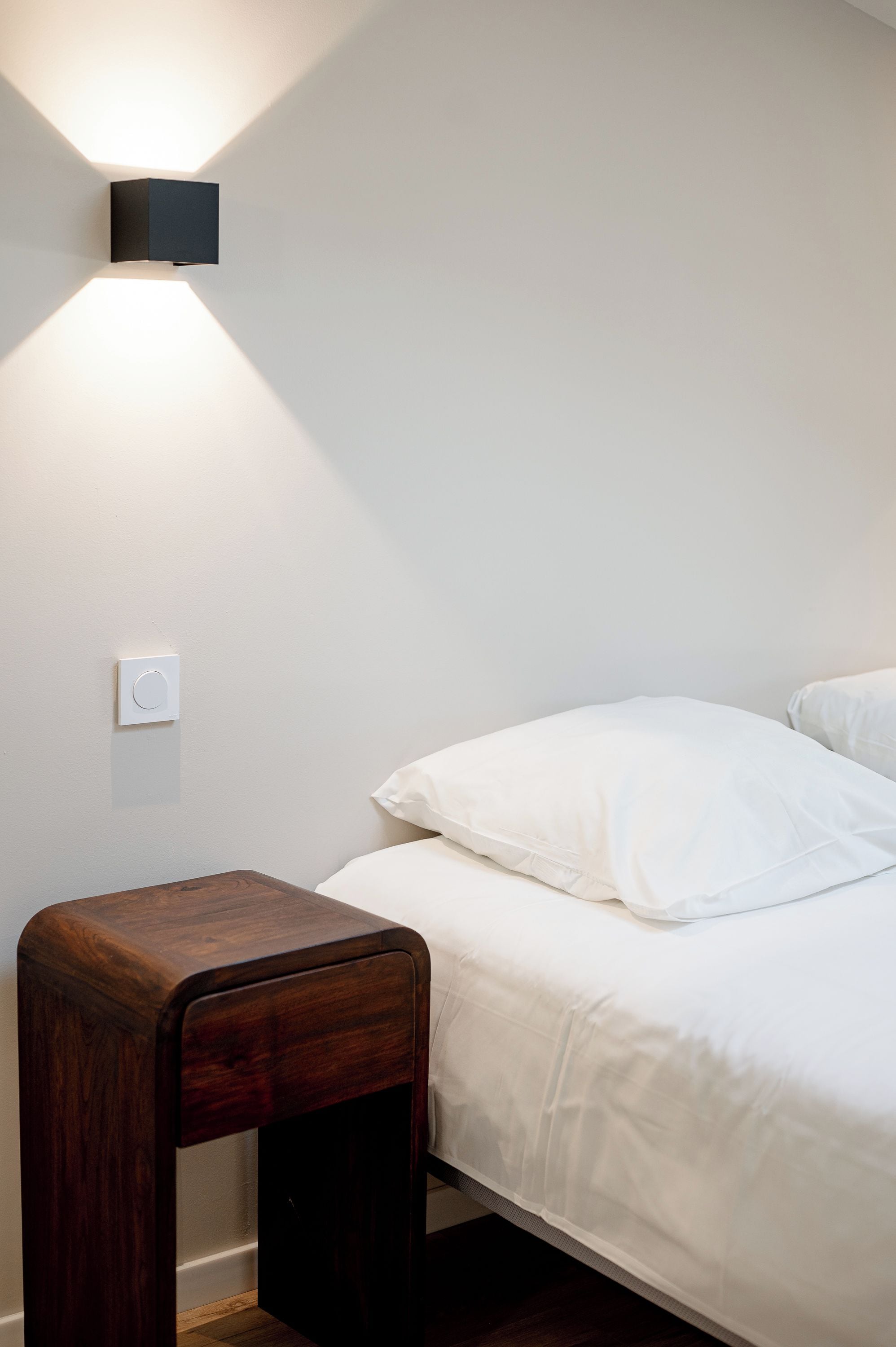 Een slaapkamer met een bed, een nachtkastje en een wandlamp.