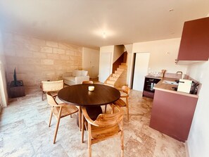 A dining area with a round table and chairs, a kitchen with a counter and appliances, and a staircase leading to another level.