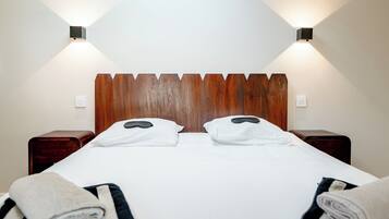A neatly made bed with white linens, two pillows, and a wooden headboard. There are two bedside tables with lamps on either side.