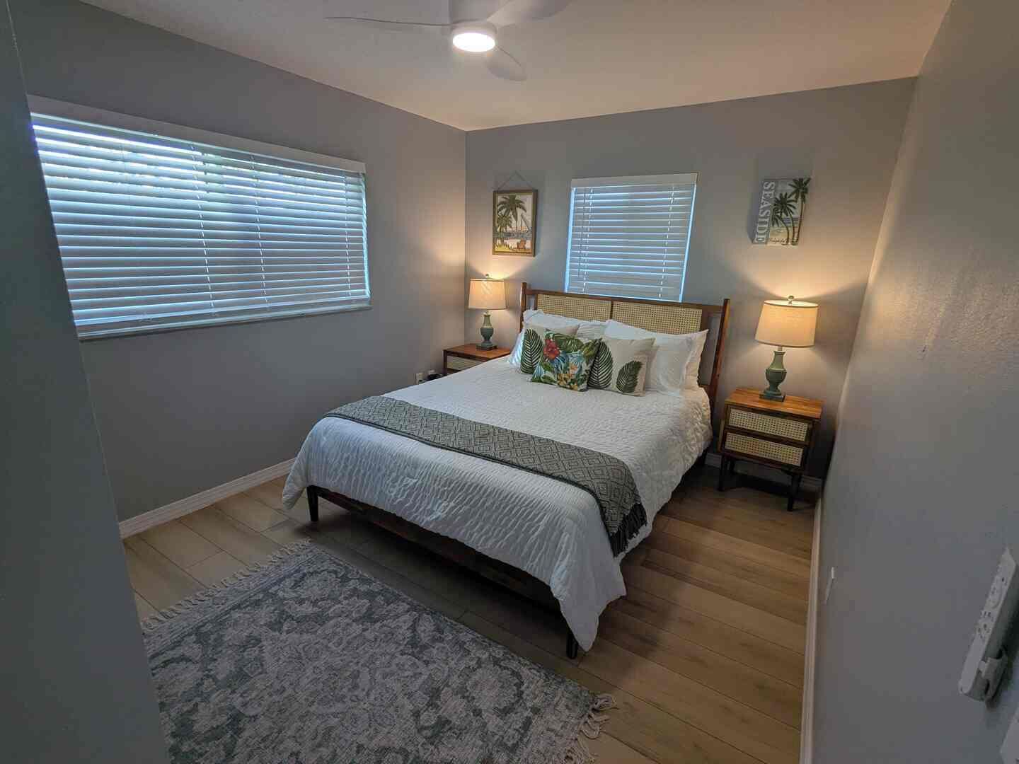 A bedroom with a bed, two bedside lamps, a ceiling fan, and a window with blinds.