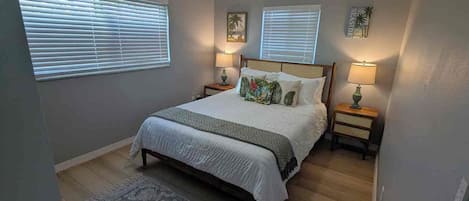 Une chambre à coucher avec un lit, deux lampes de chevet, un ventilateur de plafond et une fenêtre avec des stores.