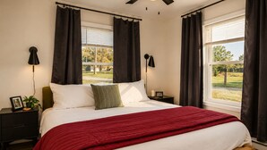 Un dormitorio con una cama, una mesita de noche, una lámpara y vistas al exterior.