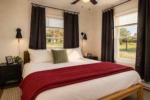 A bedroom with a bed, a nightstand, a lamp, and a view of the outdoors.
