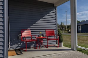 A covered porch with two red metal chairs and a small table, a yellow lantern, and a welcome mat. - Last Light Outdoor Retreat | Seneca Modern | Seneca Wine Trail | Firepit (Lodi)