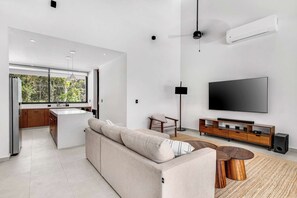 A modern living space with a kitchen, a sofa, a TV, and a dining area.