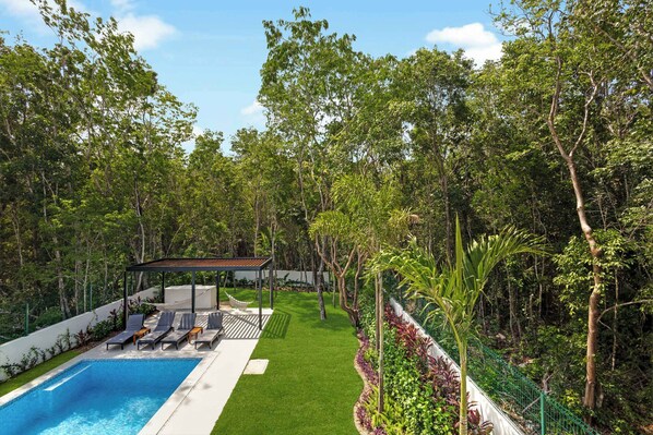 A swimming pool with lounge chairs, a covered seating area, and a lush garden with various plants.