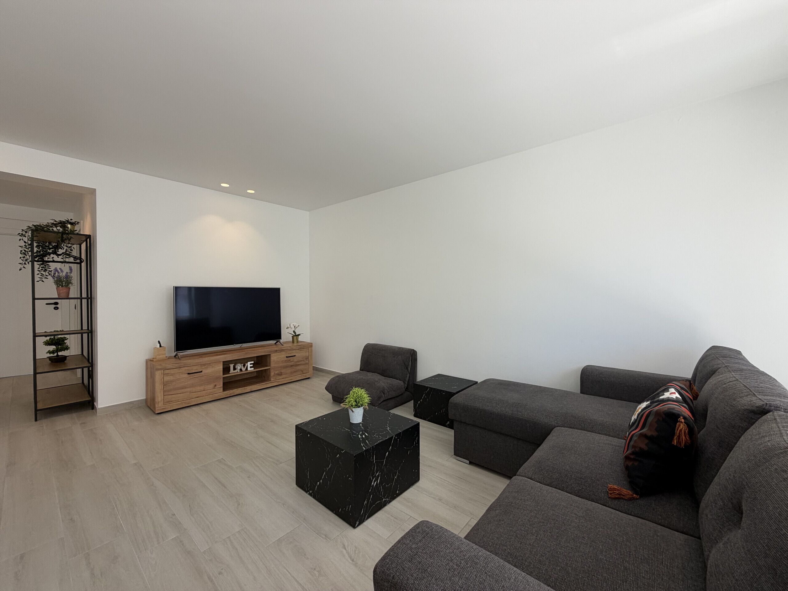 Ein modernes Wohnzimmer mit einem Flachbildfernseher, grauen Sofas, einem schwarzen Couchtisch und einem Holz-TV-Schrank.