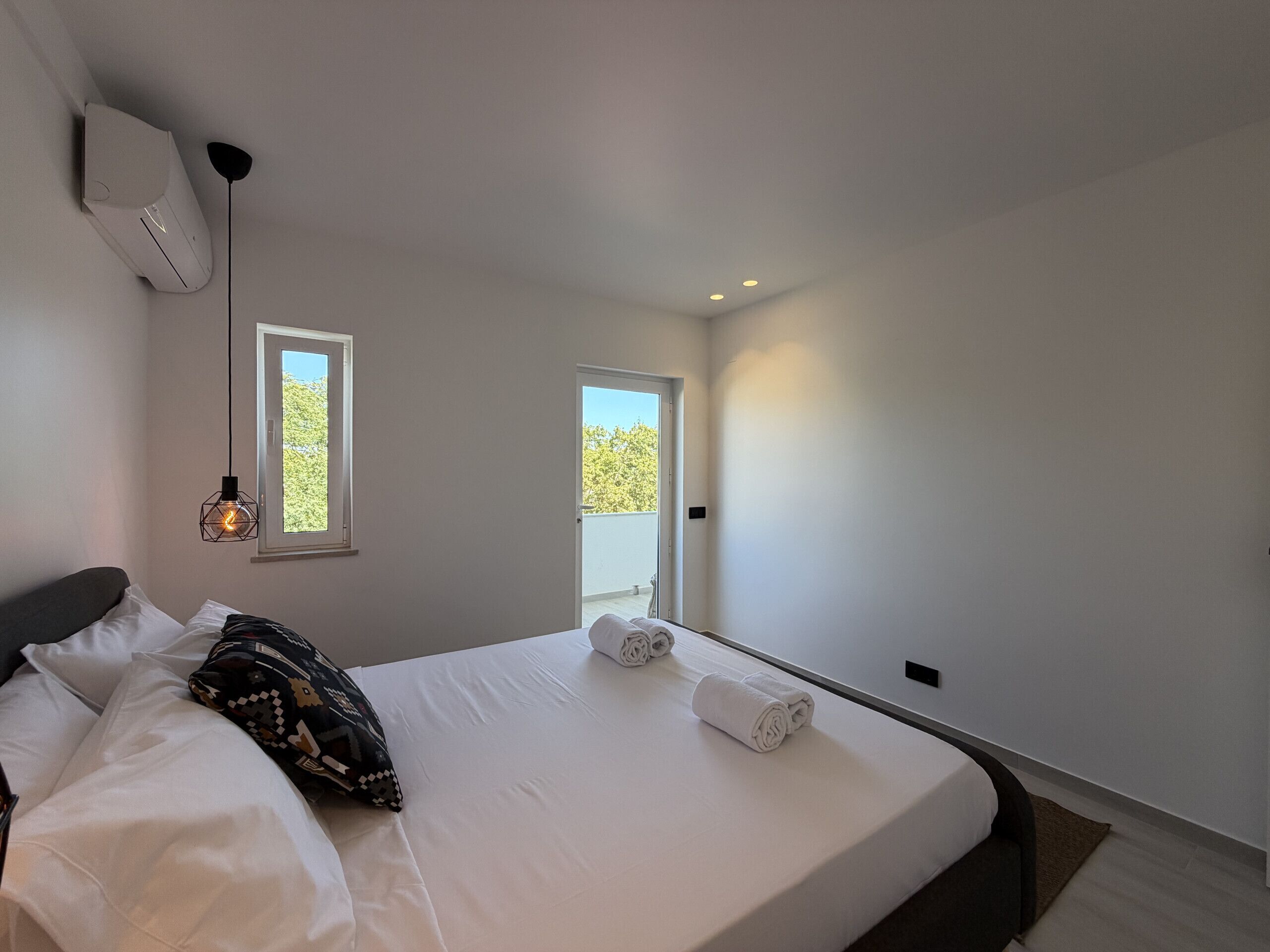 Une chambre moderne avec un grand lit, deux fenêtres et une porte donnant sur un espace extérieur.