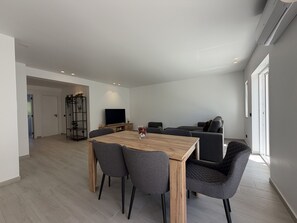 A modern living room with a wooden dining table, grey upholstered chairs, a black sofa, and a television. - Agua Plaza T2 With Pool AC (Albufeira)