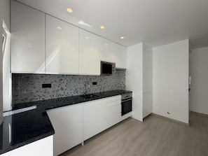 A modern kitchen with white cabinetry, a granite countertop, and a built-in microwave. - Agua Plaza T2 With Pool AC (Albufeira)