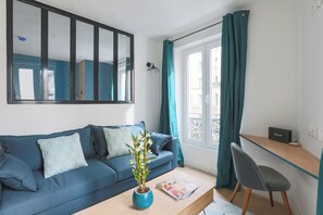 A modern living room with a blue sofa, a coffee table, a potted plant, and a desk with a chair. - MATISSIA Monceau (Paris)