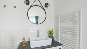 Un baño con un lavamanos blanco, encimera negra y un espejo encima. Hay un perchero en la pared y un radiador blanco.