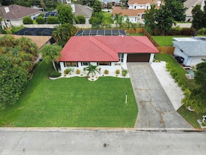 A residential house with a red roof, a driveway, and a well-maintained lawn. - Tropicana Bungalow with Heated Pool, Pool Table & Tropical Vibes (Fort Myers)