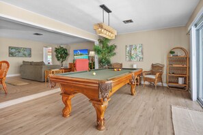 A spacious living area with a pool table, comfortable seating, and a large window providing natural light. - Tropicana Bungalow with Heated Pool, Pool Table & Tropical Vibes (Fort Myers)