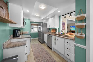 A modern kitchen with white cabinets, a stainless steel refrigerator, and a granite countertop. - Tropicana Bungalow with Heated Pool, Pool Table & Tropical Vibes (Fort Myers)