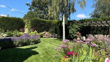 Um jardim bem cuidado, com diversas plantas e flores, gramado aparado e uma pérgola de madeira.
