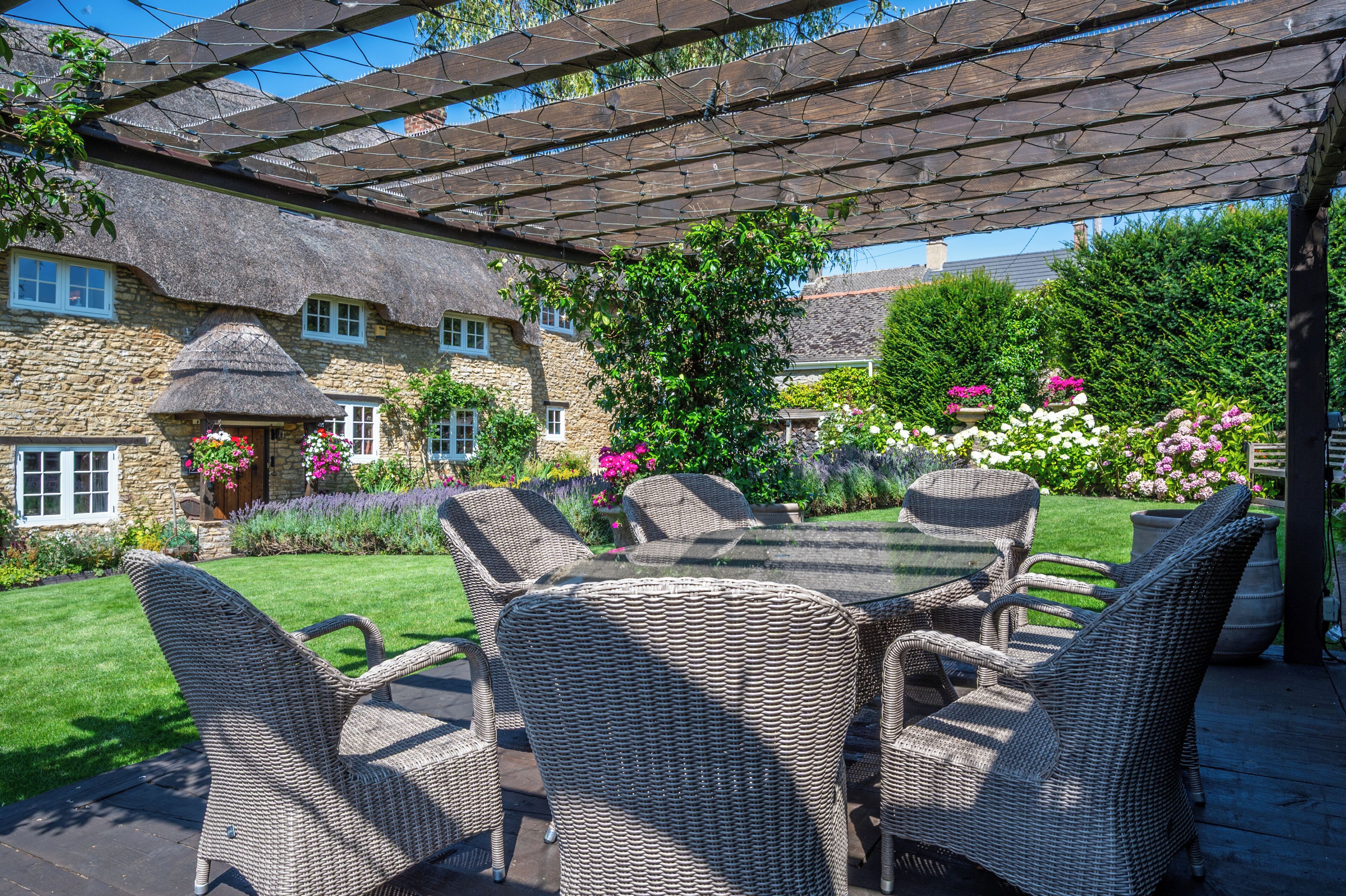 Een terras met rieten meubels, een stenen gebouw en een tuin vol bloemen.