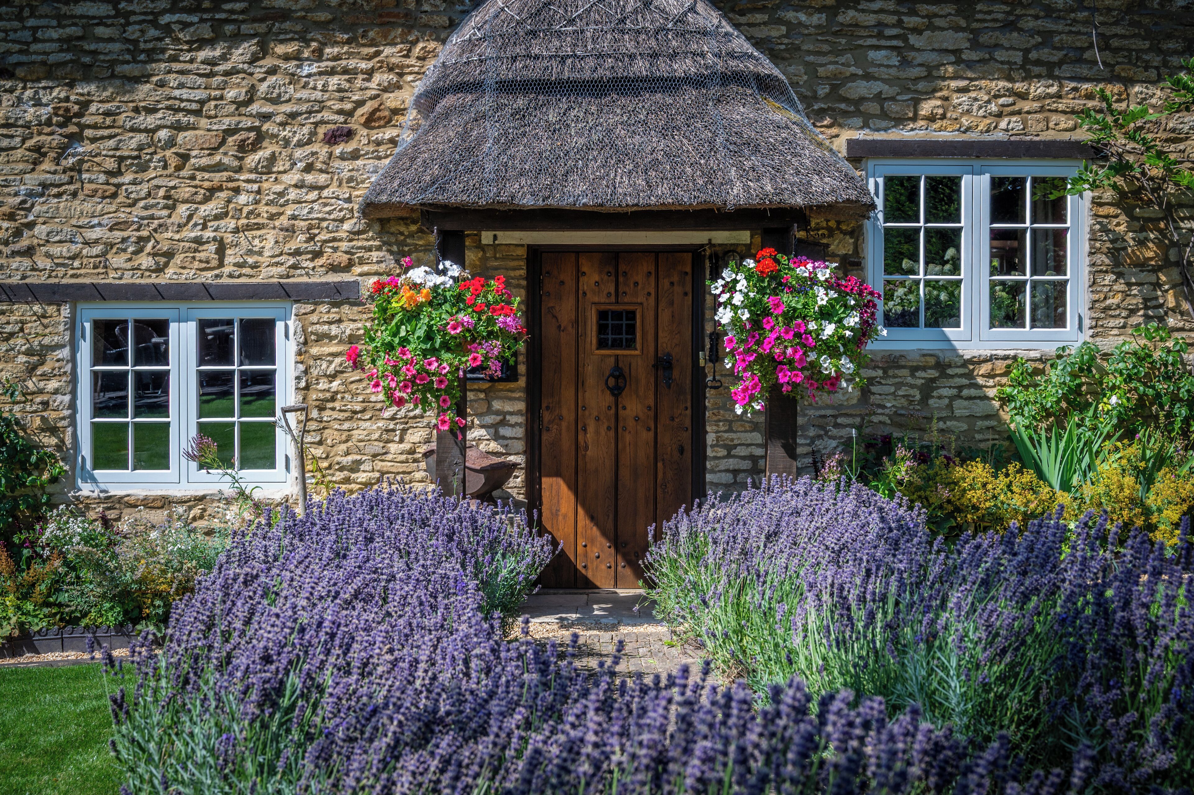 A stone cottage with a thatched roof, a wooden door, and flower boxes on the windows.
