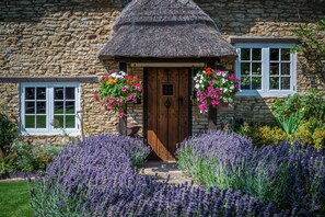 A stone cottage with a thatched roof, a wooden door, and flower boxes on the windows. - Gorgeous character Cottage on the edge of the Cotswolds (Middle Barton)