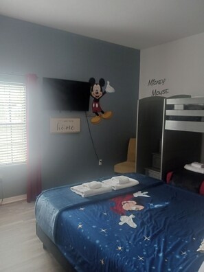 Une chambre avec un lit, un autocollant mural à l’effigie de Mickey Mouse, une pancarte sur laquelle on peut lire « C’est bon de rentrer à la maison » et une fenêtre avec des stores.