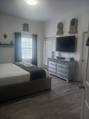 A bedroom with a bed, dresser, TV, and a window with curtains. - Cozy 2-bedroom condo in peaceful Kissimmee with AC and gym (Kissimmee)