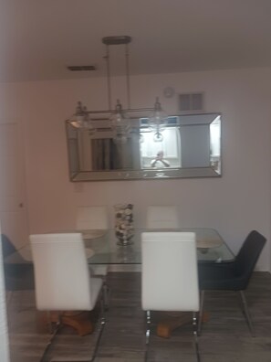 A dining area with a glass table, white chairs, a large mirror, and a chandelier. - Cozy 2-bedroom condo in peaceful Kissimmee with AC and gym (Kissimmee)