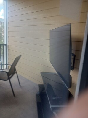 A room with a large flat-screen TV mounted on the wall, a chair, and a small table. - Cozy 2-bedroom condo in peaceful Kissimmee with AC and gym (Kissimmee)